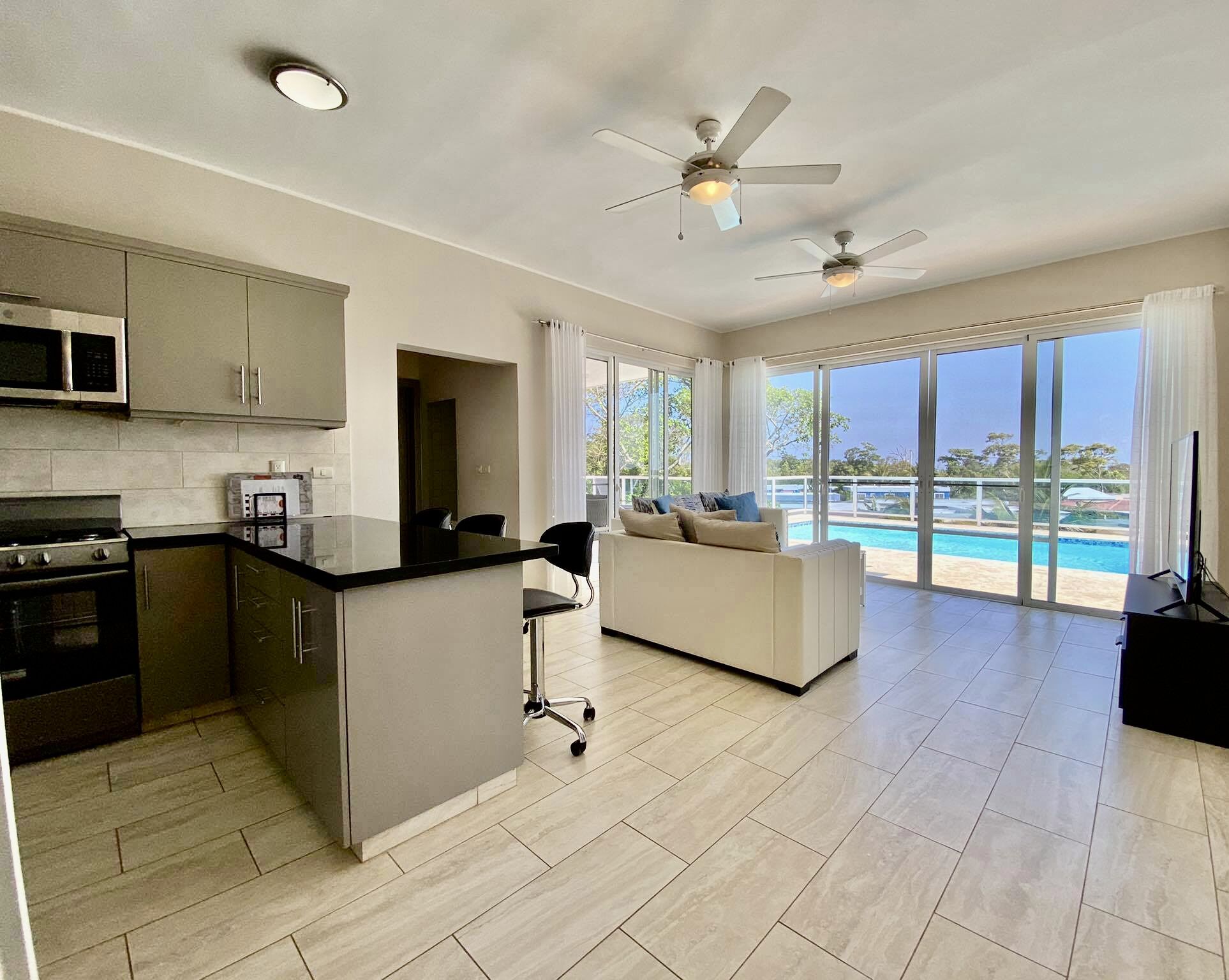 Una cocina moderna con una isla central, un área de comedor con sofá y un amplio ventanal corredero que da a una piscina.