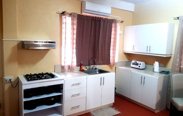 Una cocina compacta con alacenas blancas, estufa a gas, lavamanos y tostadora.