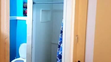 Ein Badezimmer mit blauer Wand, einer weißen Toilette, einer Dusche mit blau gemustertem Vorhang und einem an der Wand befestigten Feuerlöscher.