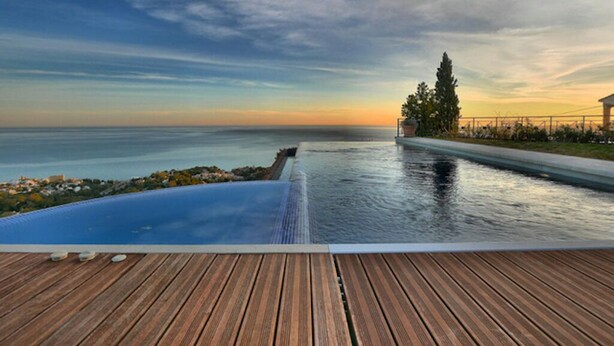 A wooden deck with an infinity pool overlooking the sea.