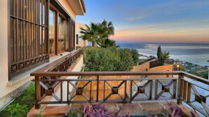 A balcony with a view of the sea, a railing, and some greenery.