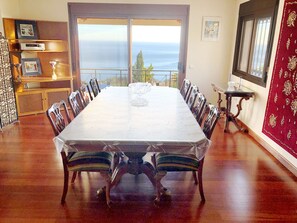 Une salle à manger avec une grande table et des chaises, une vue sur l’océan et un mur décoré d’un motif rouge.