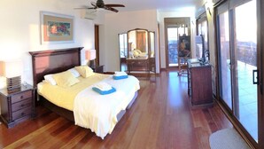 A hotel room with a large bed, a desk, a chair, a mirror, and a balcony with a view.