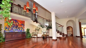 A spacious foyer with a wooden floor, a staircase, and a large colorful painting.