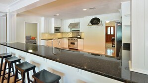 Una cocina moderna con armarios blancos, encimera de granito negro y campana extractora de acero inoxidable. Hay cuatro taburetes de bar en la encimera.