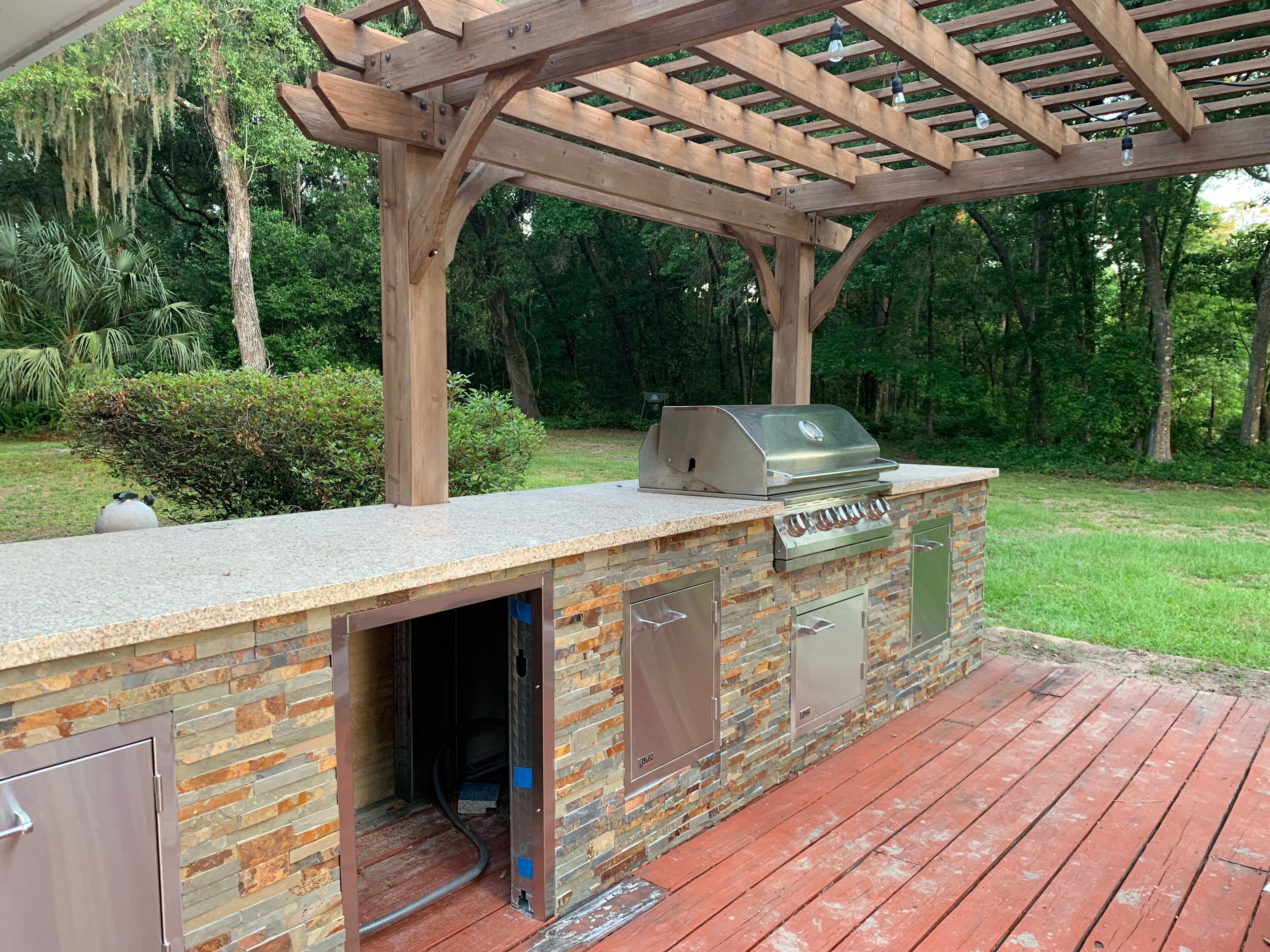 An outdoor kitchen with a grill, built-in cabinets, and a pergola overhead.
