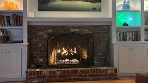 Una chimenea con detalles de ladrillo, un cuadro de paisaje enmarcado sobre ella, y estantes con libros y objetos decorativos.