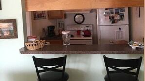 A kitchen with a wooden countertop, two black chairs, a refrigerator with photos, and a blender. - Discounted 30 Day Minimum Stay. 2bd. 2bth. Private 2nd floor Condo & balconies. (Corpus Christi)