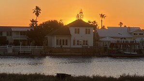 A waterfront property with a house featuring a large balcony, a dock, and a view of the sunset over the water. - Discounted 30 Day Minimum Stay. 2bd. 2bth. Private 2nd floor Condo & balconies. (Corpus Christi)