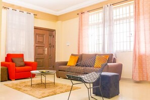 A living room with a sofa, a chair, a coffee table, and a door. - Oakhills Homes (Taifa)