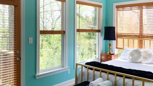 Un dormitorio con cama, un banco, una araña y ventanas amplias con persianas.