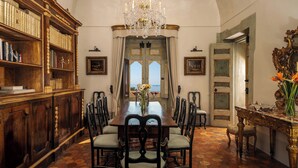 Un comedor formal con una gran mesa de madera, sillas, una araña y una estantería.