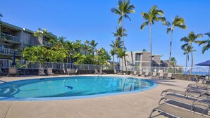 A swimming pool with lounge chairs, palm trees, and a building with balconies.