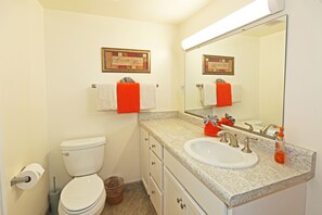 A bathroom with a toilet, sink, and a large mirror. There are towels hanging on the wall and a trash can. - 🌴Newly updated ocean view condo located close to the ocean🌴 (Kailua Kona)