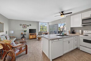 A modern kitchen with a central island, white cabinetry, and a dining area with wicker furniture.