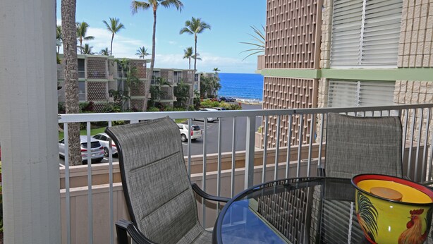 Un balcon offrant une vue sur l’océan, les palmiers et un immeuble à la façade quadrillée.