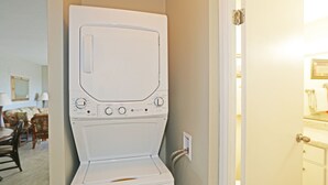 Une machine à laver et un sèche-linge blancs à chargement frontal, dans une pièce où l’on aperçoit un coin repas à l’arrière-plan.