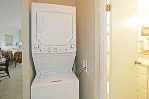 Une machine à laver et un sèche-linge blancs à chargement frontal, dans une pièce où l’on aperçoit un coin repas à l’arrière-plan.