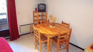 A wooden dining table with six chairs, a small wooden shelf with a television, and a vase with dried plants. - 300m from ski slopes, 1st floor, balcony, 24m², Vars (Vars)