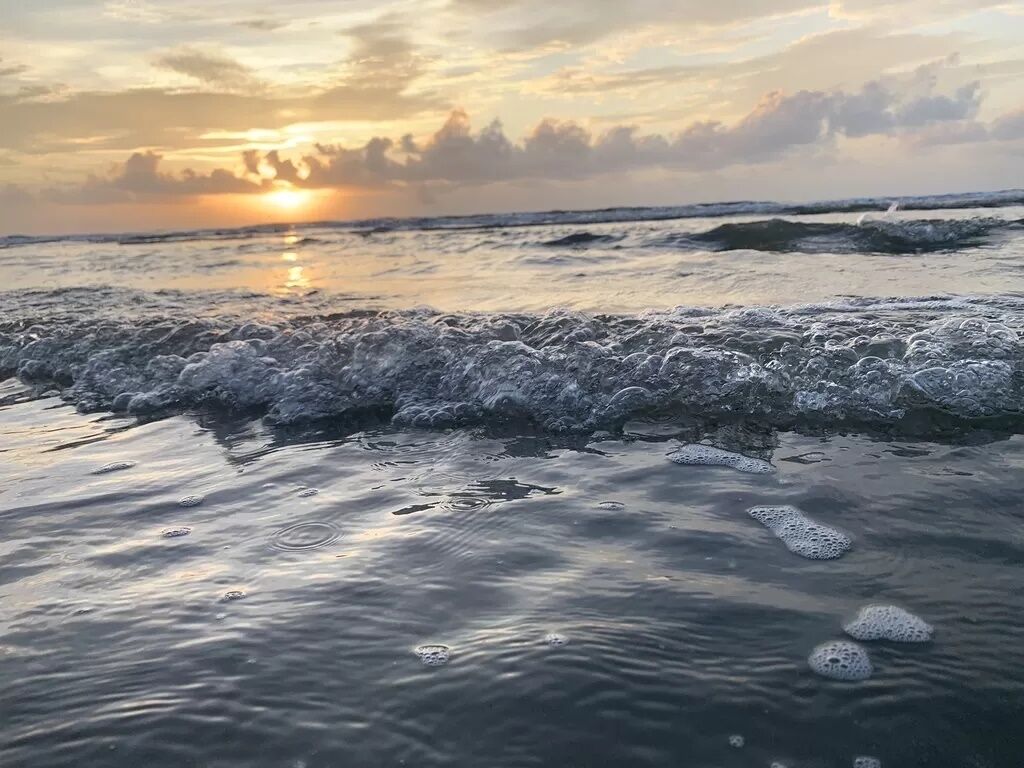 Escena de playa con olas y un atardecer.