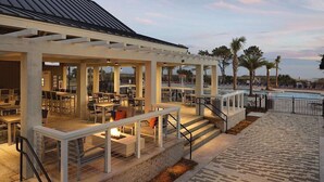 Un patio al aire libre con mesas y sillas, piscina y palmeras.