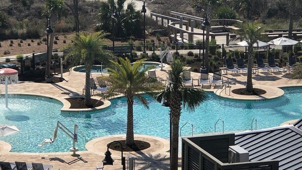 Un resort con piscina, sillas de descanso y vista a la playa.