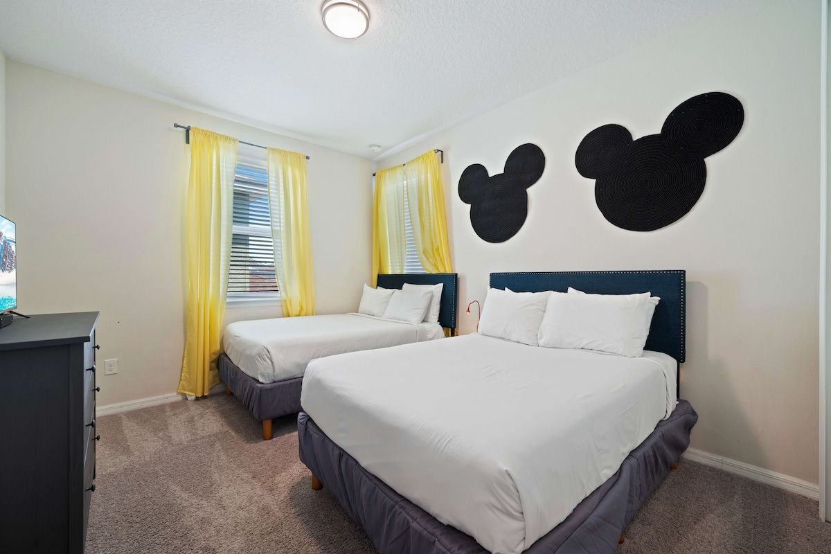 Quarto de hotel com duas camas, uma escrivaninha e uma decoração de parede do Mickey Mouse.