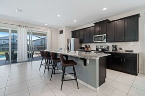 A modern kitchen with dark cabinets, a large island with bar stools, and a sliding glass door leading to an outdoor area.