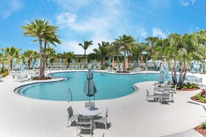 Un espace piscine agrémenté de chaises longues et de parasols, entouré de palmiers.