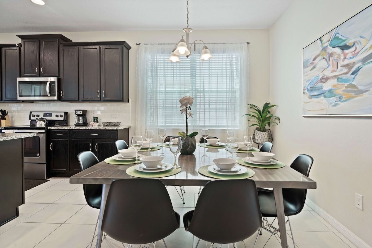 A modern kitchen with dark cabinets, a microwave, and a dining area with a table set for four.