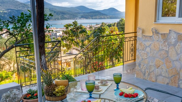A balcony with a table set for a meal, overlooking a scenic view of a lake and mountains. - KYVELI SUPERB SEA VIEW APARTMENT (ΑΡΓΟΣΤΟΛΙ)