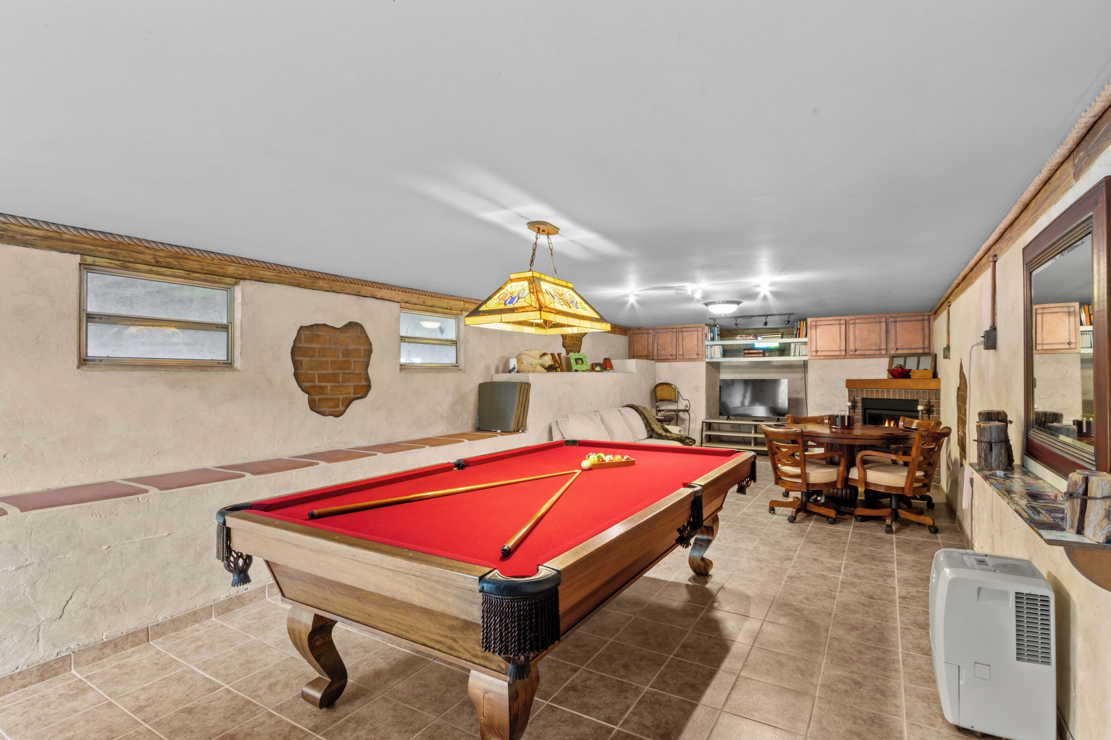 A pool table with a red felt surface, a chandelier, and a dining area with a table and chairs.