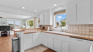 A modern kitchen with white cabinets, a wooden countertop, and a view of the outdoors. - Cottage At Sunset Key (Terrell)