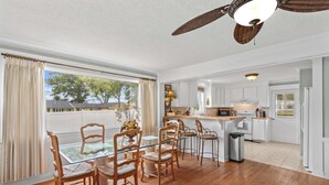 A dining area with a glass table and wooden chairs, a kitchen with white cabinets, and a ceiling fan. - Cottage At Sunset Key (Terrell)