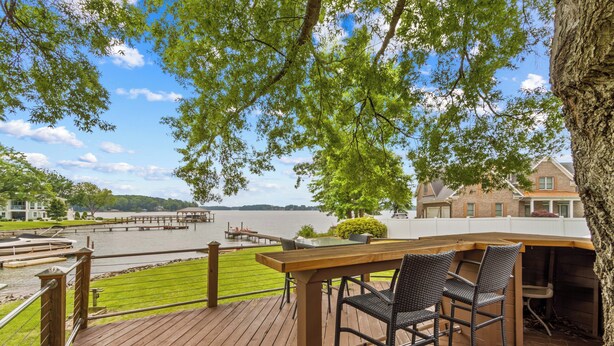 A wooden deck with a table and chairs overlooking a lake, with a house and dock in the background. - Cottage At Sunset Key (Terrell)