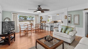 A spacious living room with a television, dining area, and a kitchen in the background. - Cottage At Sunset Key (Terrell)