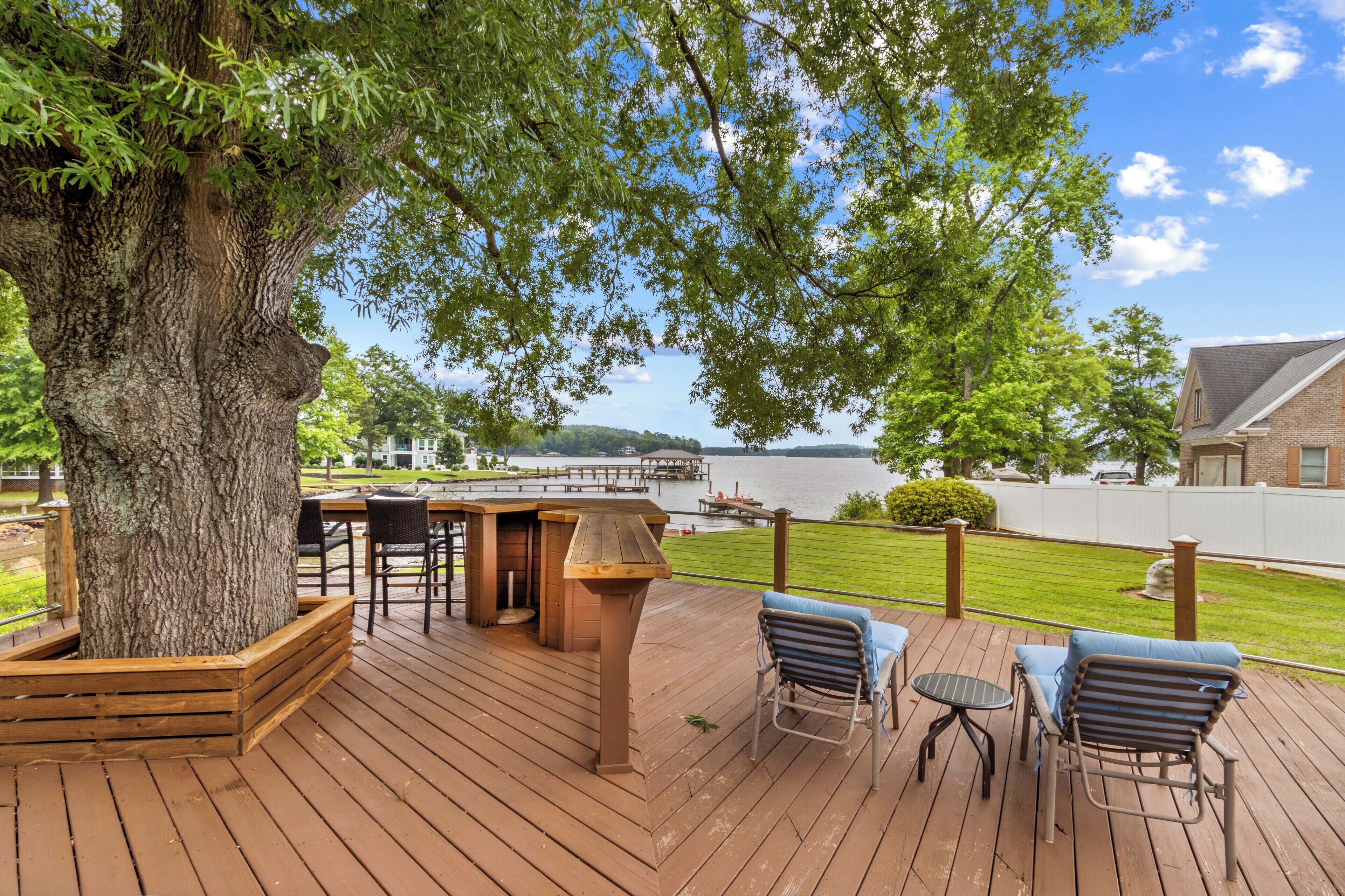 A wooden deck with outdoor seating, a large tree, and a view of a body of water.