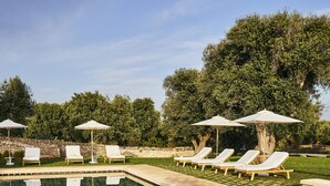 A clear swimming pool with lounge chairs and umbrellas, surrounded by greenery. - Masseria Calderisi (Fasano)