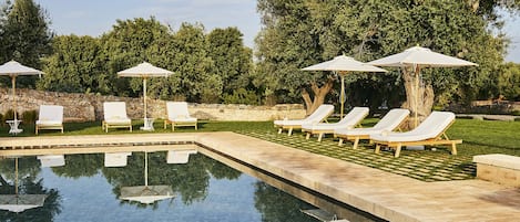Piscina cristalina con sillas de descanso y sombrillas, rodeada de follaje.