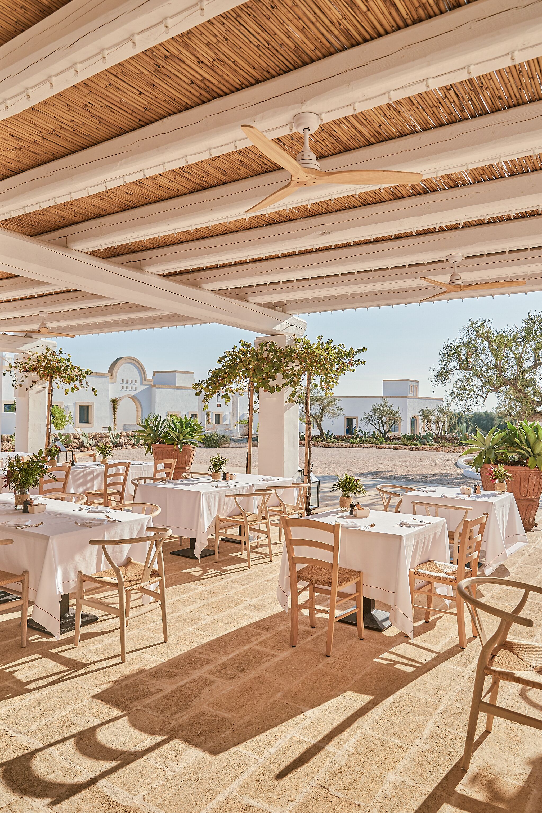 An outdoor dining area with tables and chairs, a thatched roof, and potted plants.