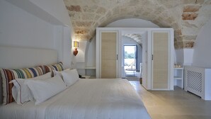 A spacious bedroom with a large bed, white walls, and a stone ceiling. - Masseria Calderisi (Fasano)