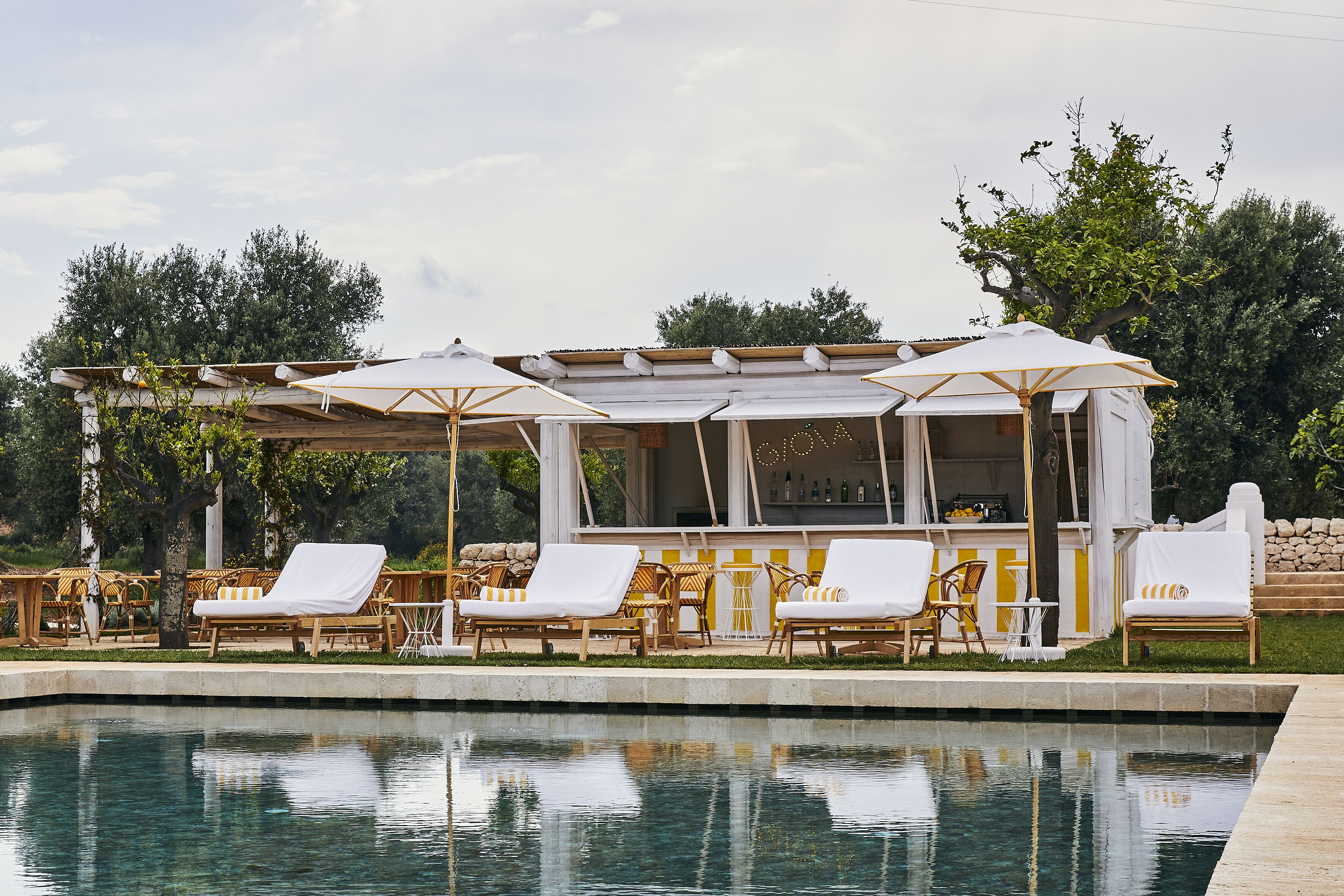 Area piscina con sedie a sdraio e ombrelloni, zona relax coperta e un bar.