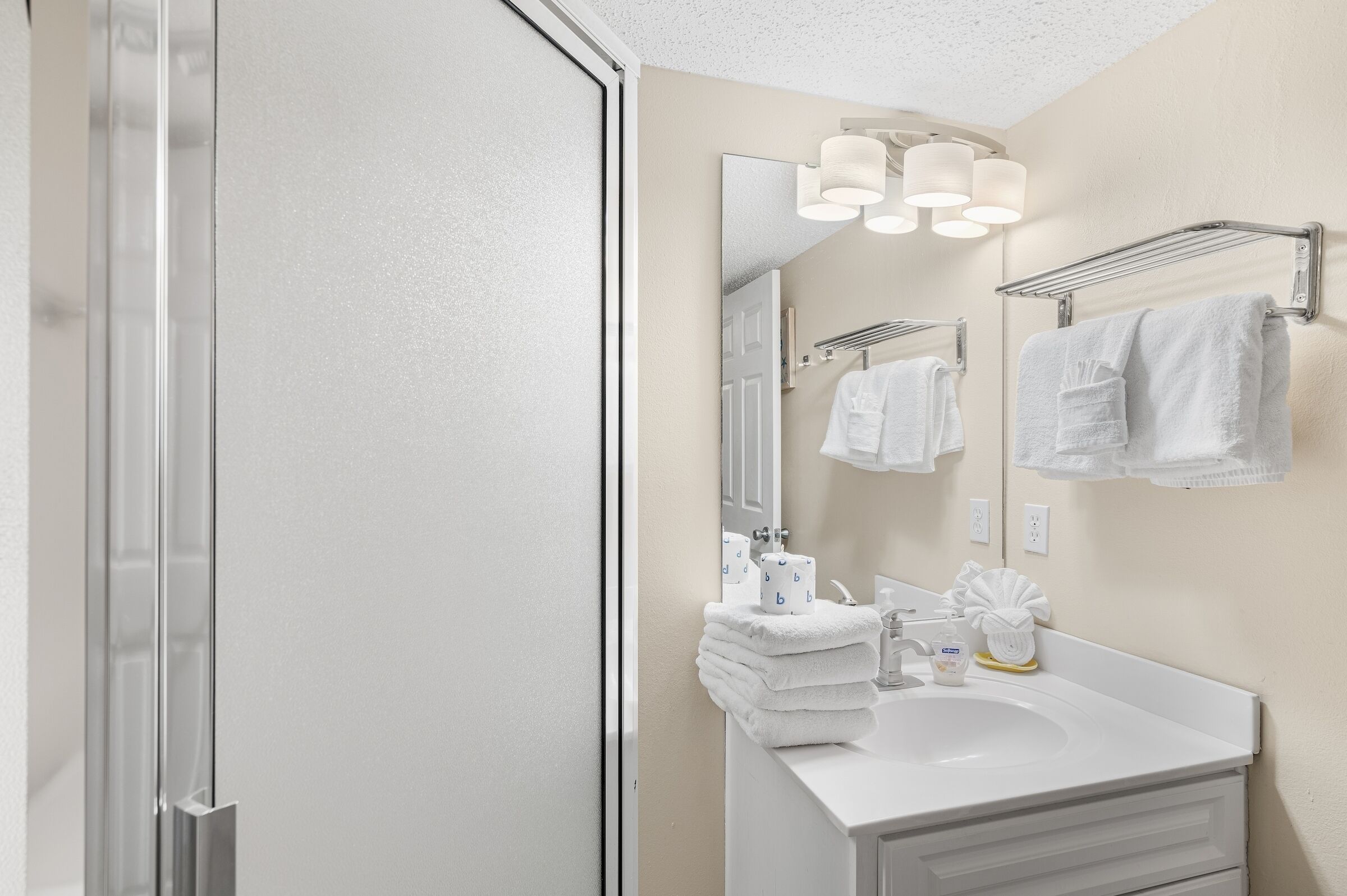 A modern bathroom with a glass shower door, a white sink, and a mirror with lights.