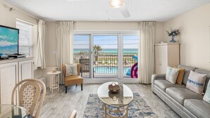 A living room with a glass table, a sofa, a TV, and a view of a pool and beach. - Pet-Friendly Gulf Front Condo • Free Beach Setup • 2 Pools + Hot Tub (Miramar Beach)