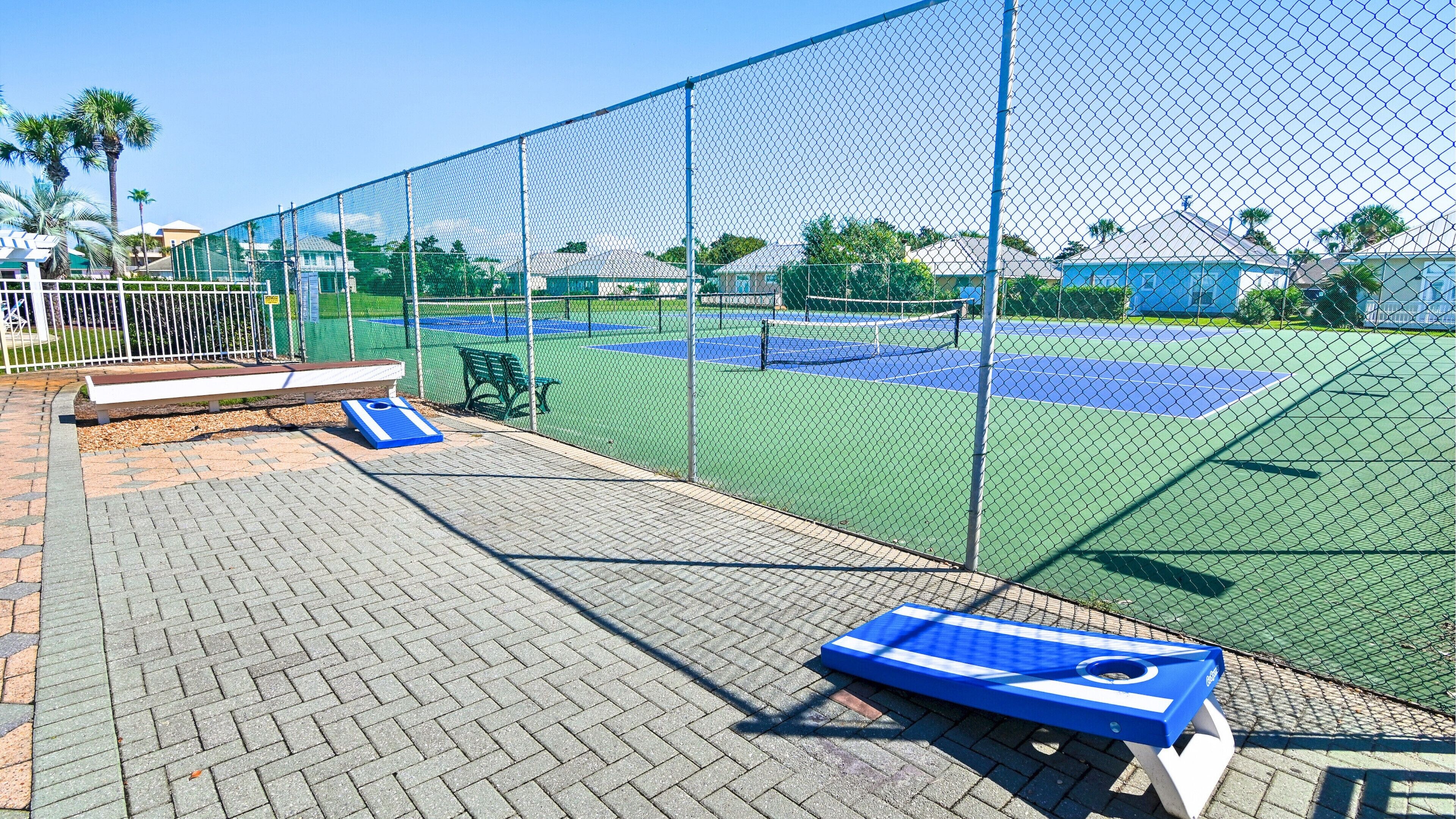 Un court de tennis entouré d’une clôture en treillis métallique, avec un banc et un petit tapis bleu.