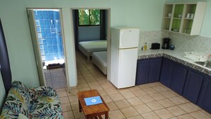 Ein kompakter Wohnbereich mit einer Couch, einem kleinen Tisch, einem Bett, einem Kühlschrank und einer Küchenzeile.