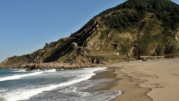 Una platja amb un penya-segada rocosa i una cadira de fusta.