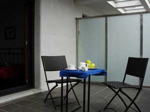 Ein kleiner Balkon mit zwei Stühlen, einem Tisch mit blauer Tischdecke und einer Schüssel mit Äpfeln.