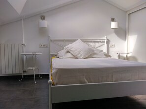 Ein weißes Bett mit Metallgestell, ein kleiner Nachttisch, eine Wandlampe und eine Heizung.