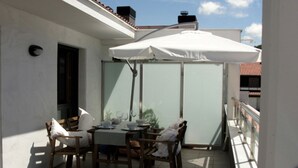 Un balcó amb taula i cadires, un para-sol blanc i vista al cel.